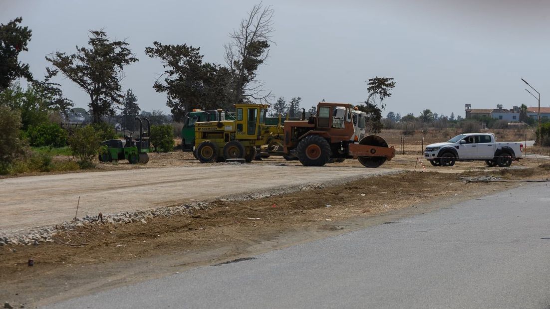Roadside construction scene with a bulldozer, dump truck, and white pickup on a dusty dirt road.