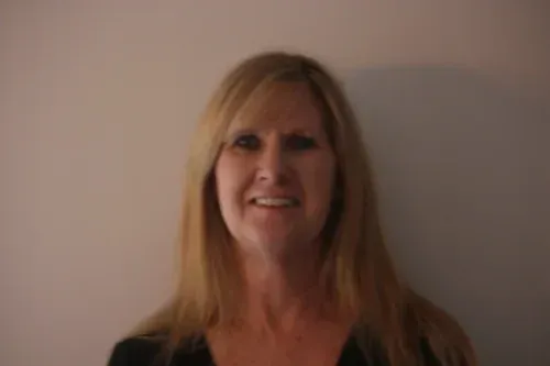 Portrait of a smiling woman with long blonde hair against a plain wall