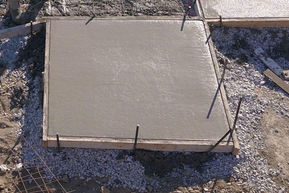 Freshly poured concrete slab with wooden formwork and rebar stakes on a gravel site