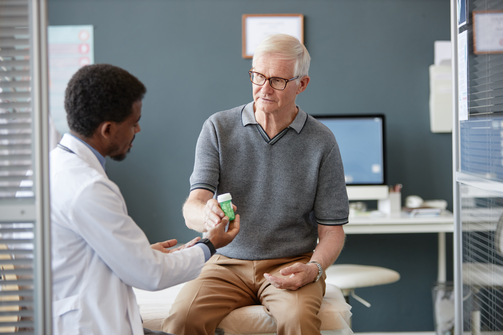 Doctor hands a pill bottle to a patient in an office setting.