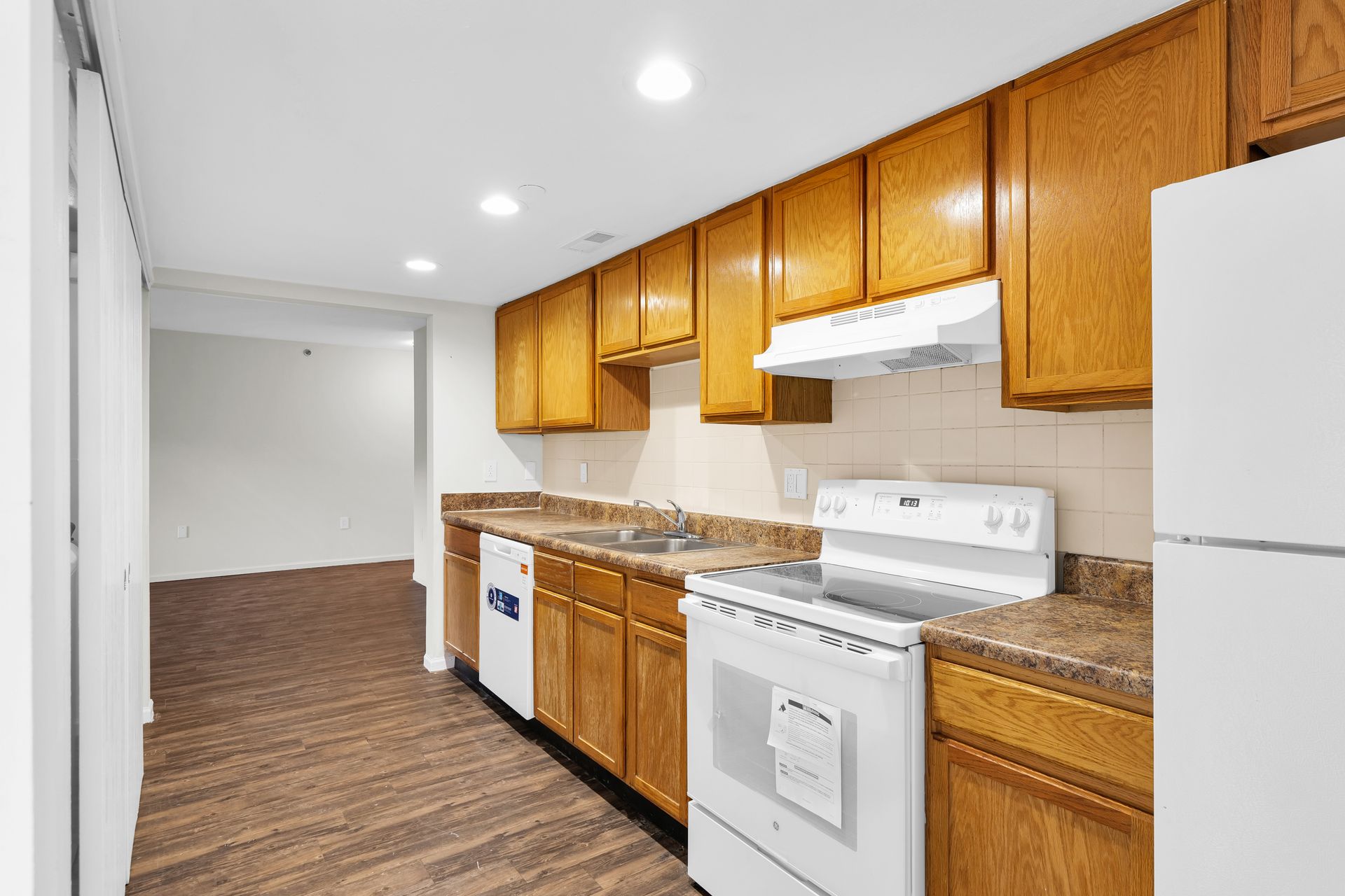 A kitchen with wooden cabinets , a stove , a refrigerator , and a sink.