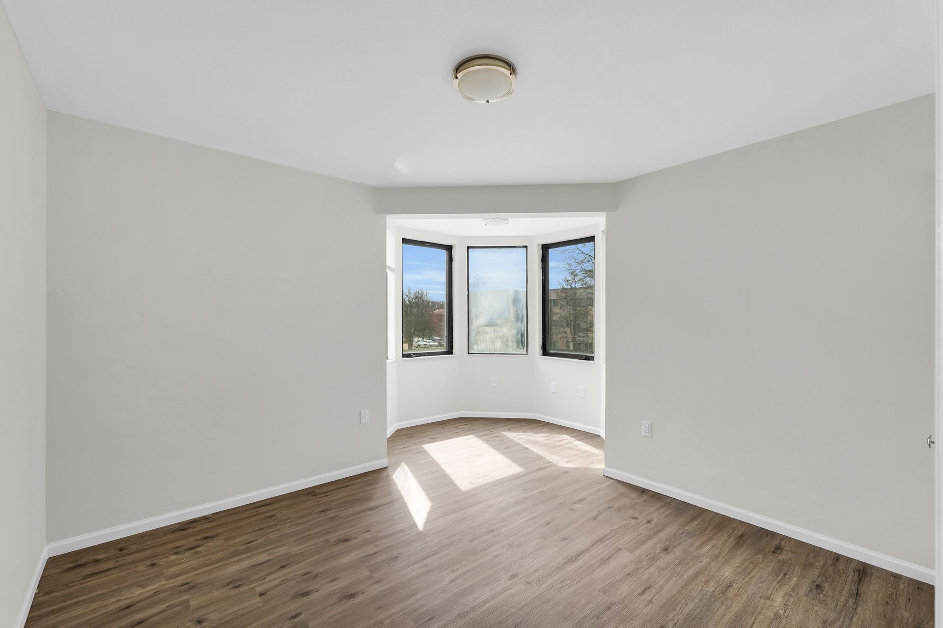 An empty room with a bay window and hardwood floors.