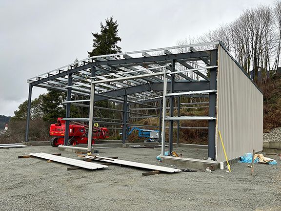 A large metal building is being built in a gravel lot.