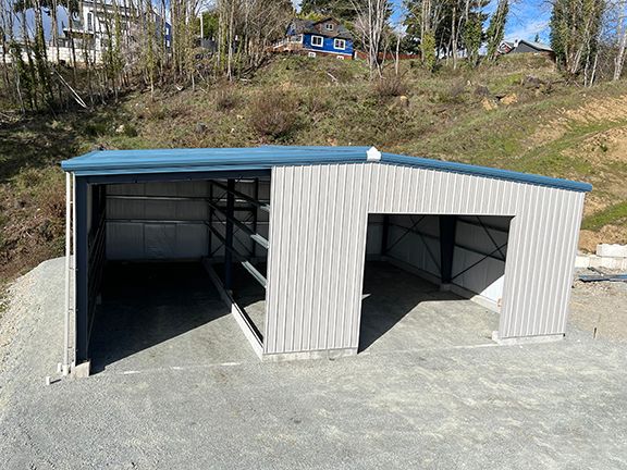 A metal building with a blue roof is sitting on top of a dirt hill.
