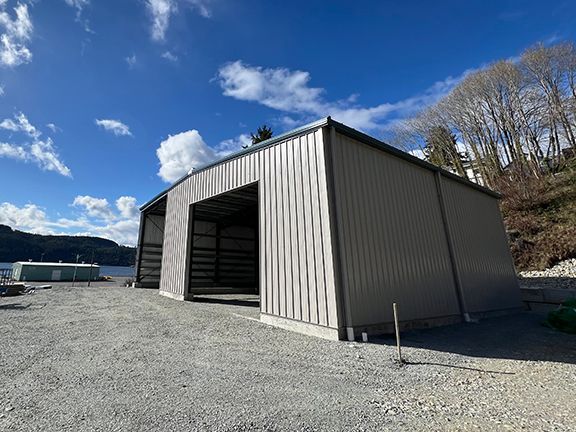 A large metal building is sitting on top of a gravel lot next to a lake.