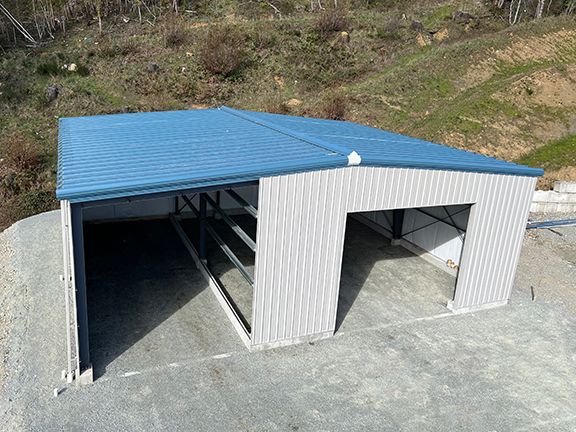 A white building with a blue roof is sitting on top of a dirt hill.