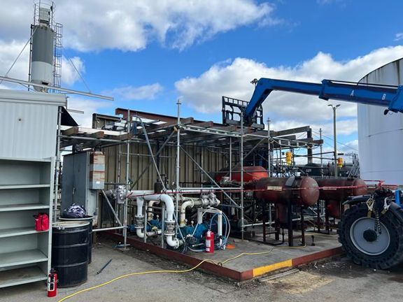 A tractor is parked in front of a building with pipes and scaffolding.