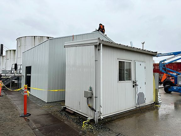 A man is working on the roof of a small white building.