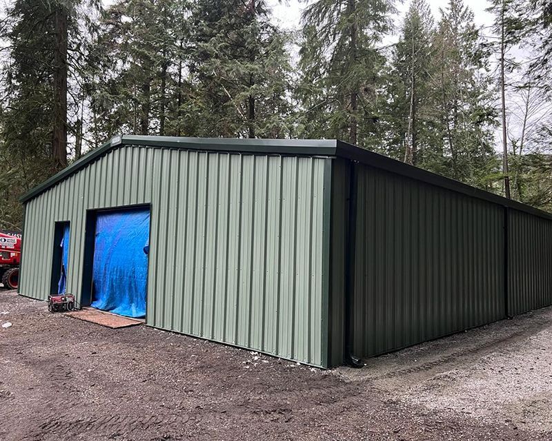 A large green metal building with a blue tarp on the side.