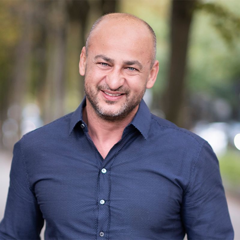 A bald man with a beard is wearing a blue shirt and smiling.