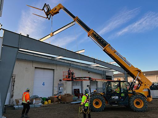 A forklift is lifting a metal structure on top of a building.
