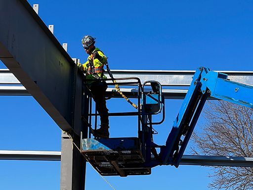 A construction worker is standing on top of a crane.