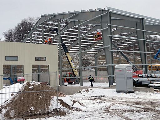 A building under construction in the snow with a portable toilet in the foreground.