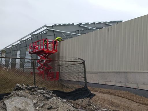 A man is standing on a scissor lift next to a building.