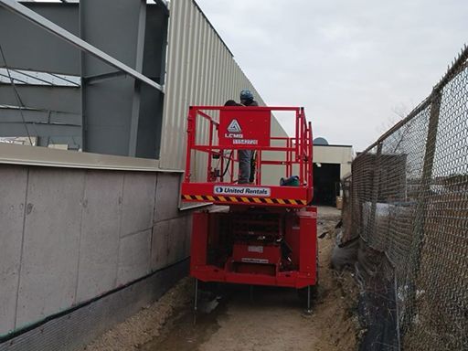 A man is standing on a red lift in front of a building.