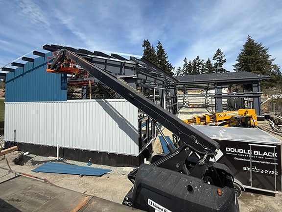 Contrasting grey and blue metal siding being added to steel building frame in BC.