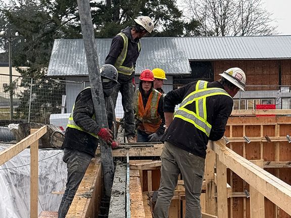 Skilled tradespeople begin to pour concrete into wooden forms at building project near Vancouver Island.
