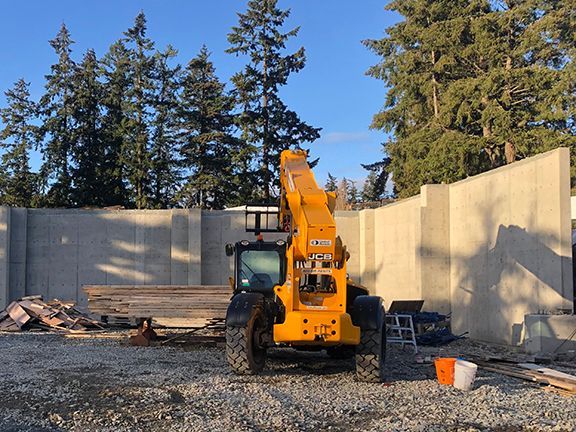 Elevator truck in front of concrete foundational wall at metal building project.