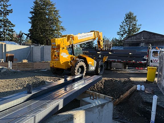 Heavy steel structural beams are lifted off truck at construction site on Salt Spring Island, BC.