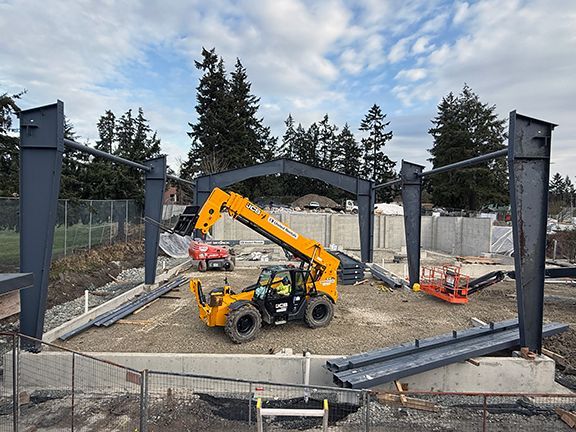 Yellow elevator lift sits in center of steel I-beam framework for industrial metal building.