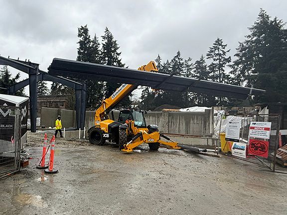 Yellow elevator truck lifts heavy steel beams at British Columbia construction site.