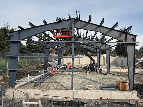 Construction workers placing metal roofing beams into place for Windsor Plywood building project.
