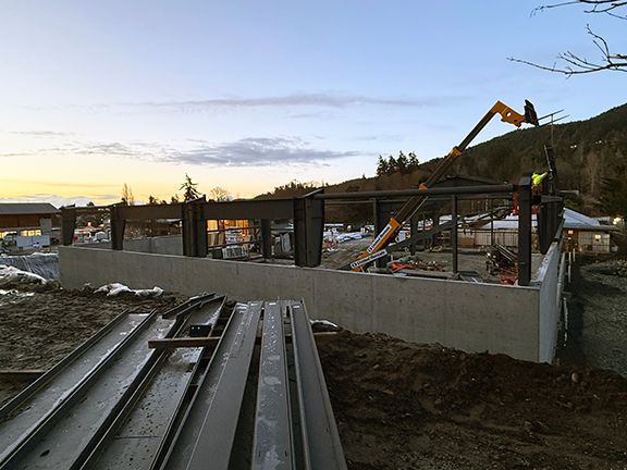 Crane lowers steel roof frame components at jobsite.