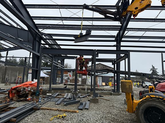 Steel roofing frames being lifted into place at an industrial warehouse construction site.