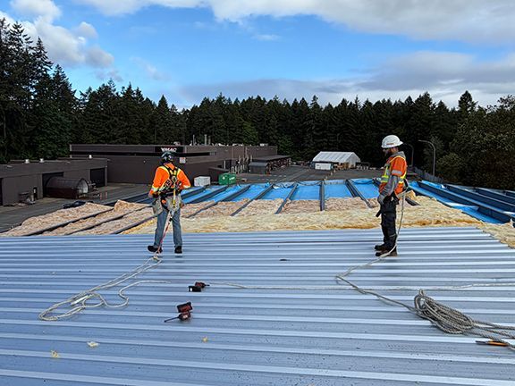 Two members of the construction crew inspect metal roofing panels.