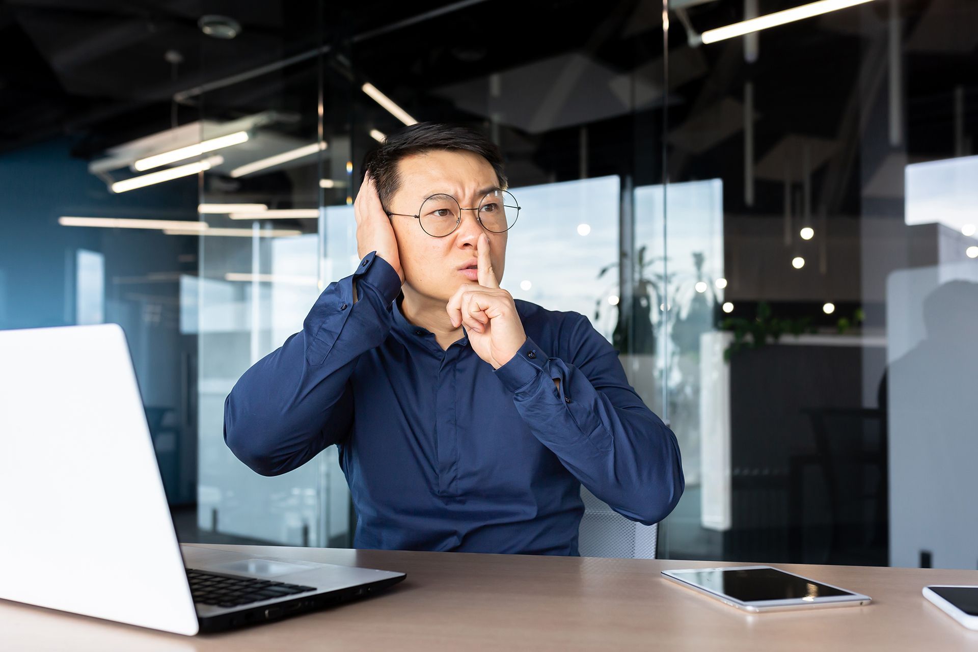 A man is sitting at a desk with a laptop and covering his ears.