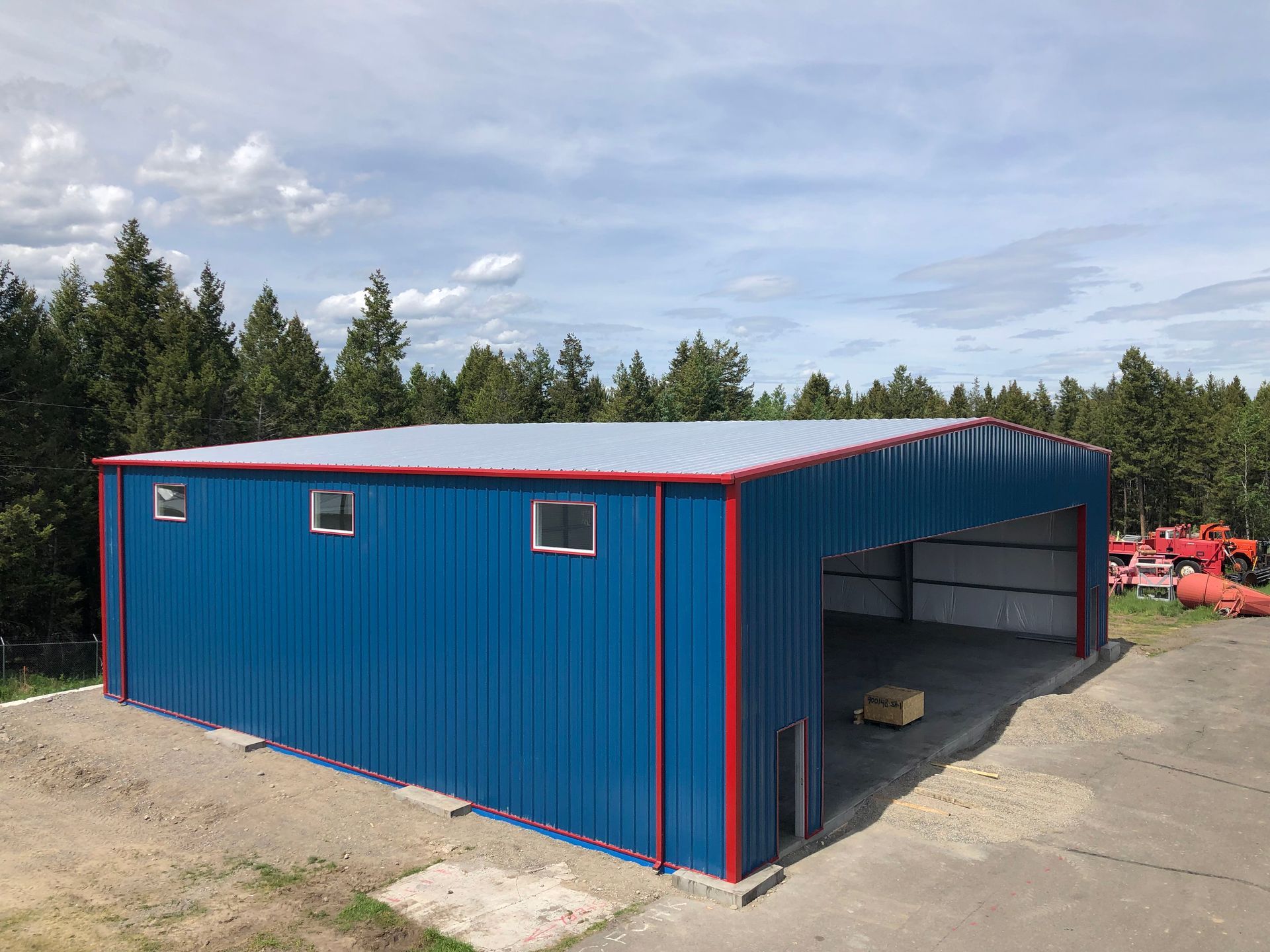 A blue metal building with a red trim is sitting on top of a dirt field.
