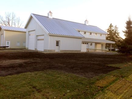 A white barn with a metal roof is sitting in the middle of a dirt field.
