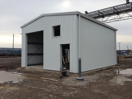 A white metal building with a large garage door is being built in a dirt field.