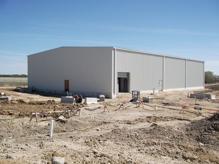 A large white building is being built in the middle of a dirt field.