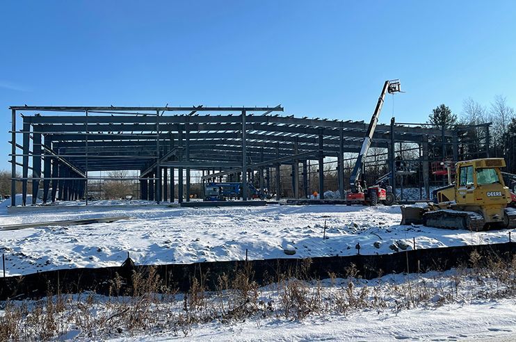 A large building under construction in the snow with a bulldozer in the foreground.