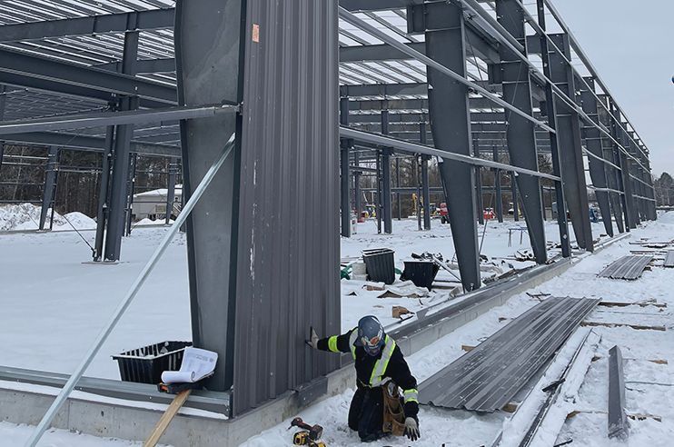 A man is kneeling in the snow next to a building under construction.
