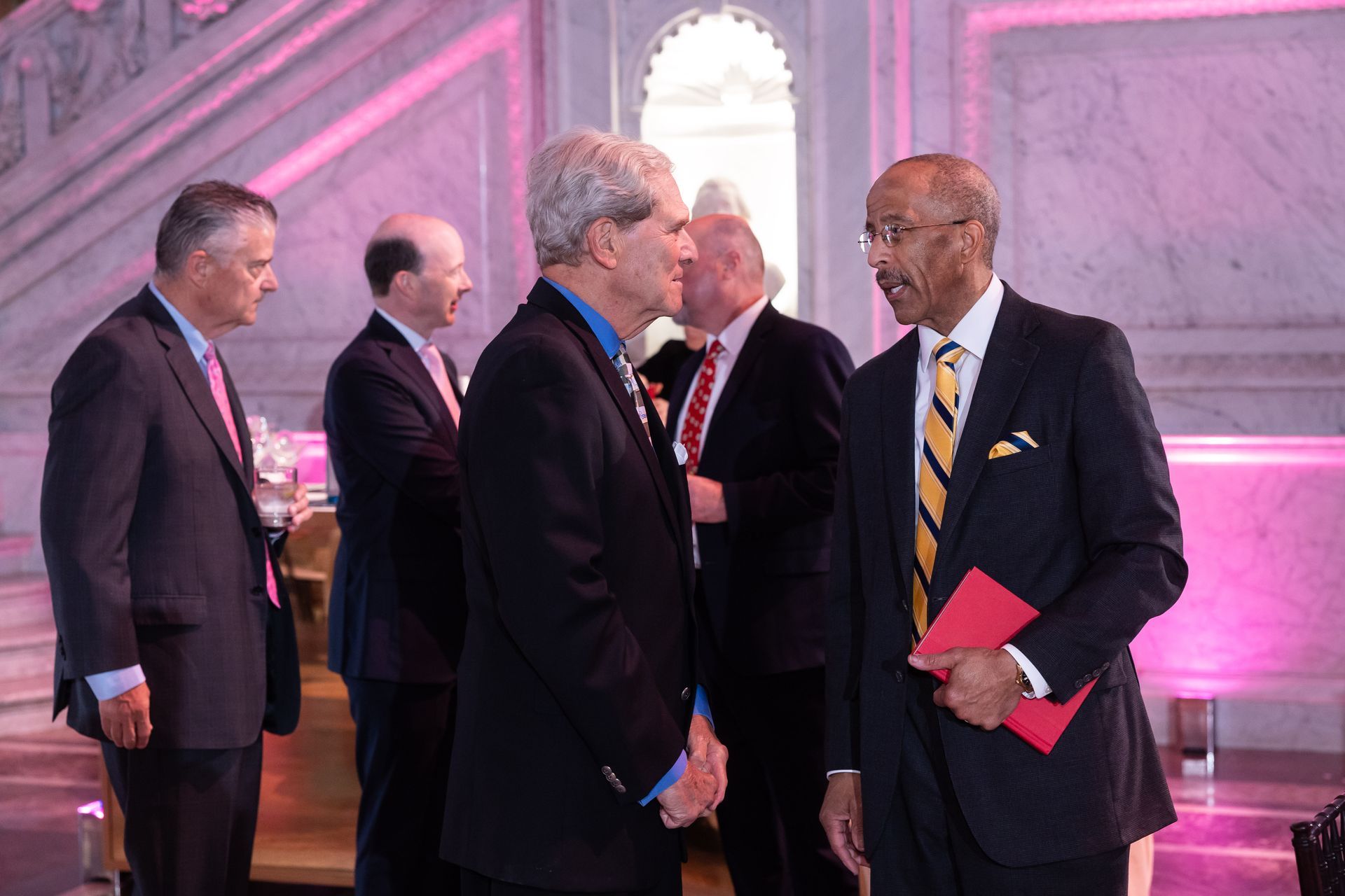 A group of men in suits and ties are standing in a room talking to each other.