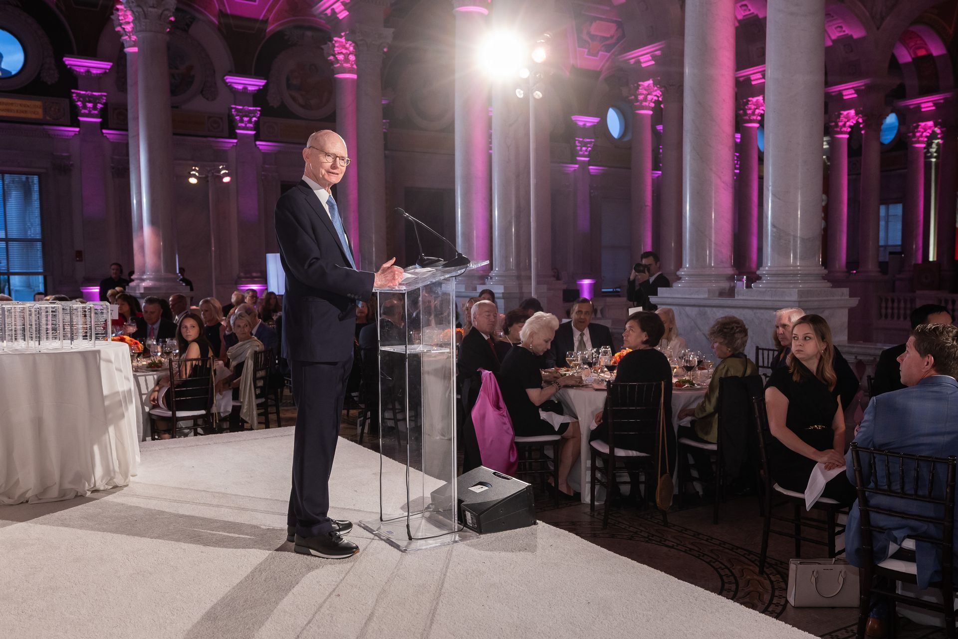 A man is standing at a podium giving a speech in front of a crowd of people.