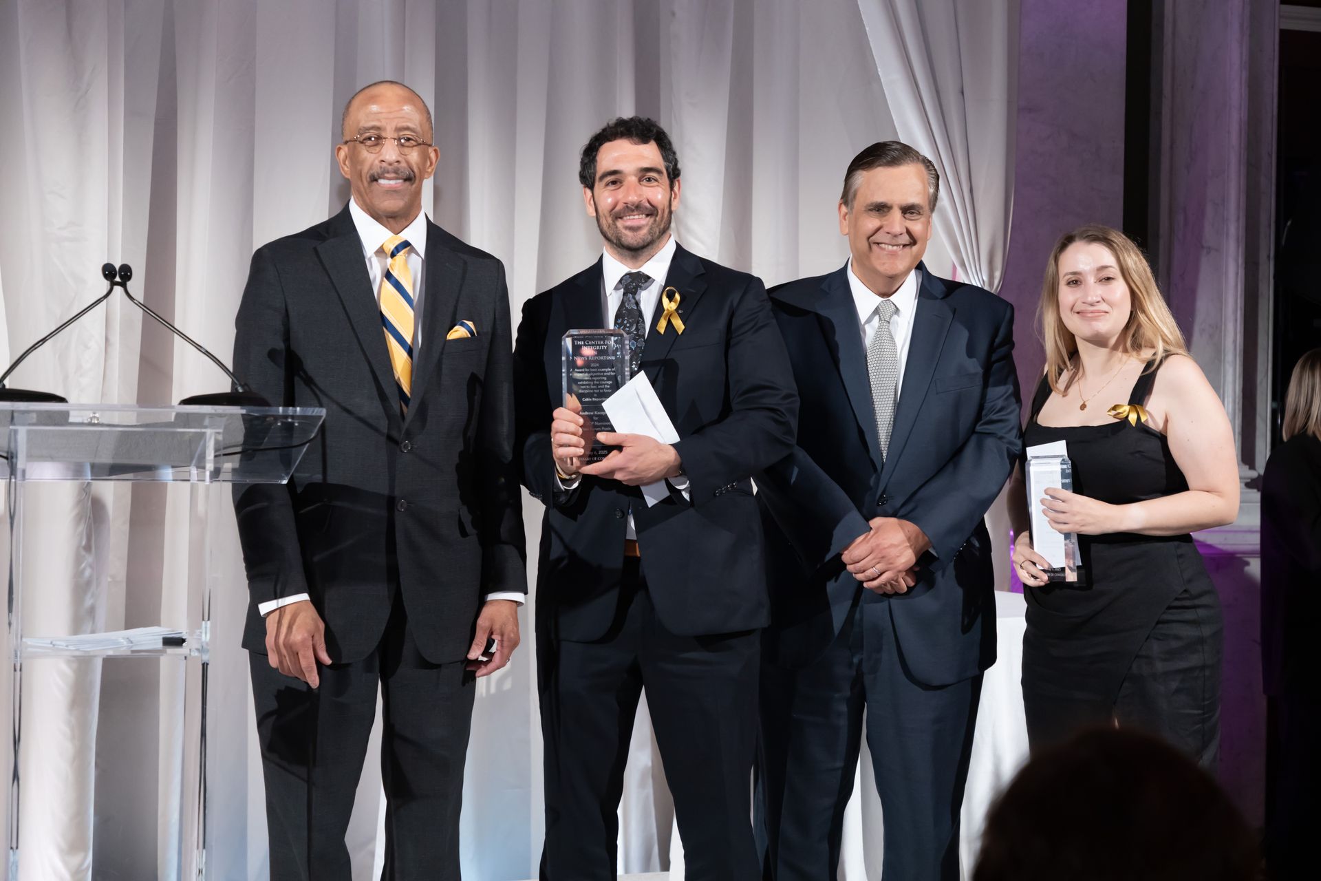 A man in a suit is holding an award while standing next to two other men and a woman.