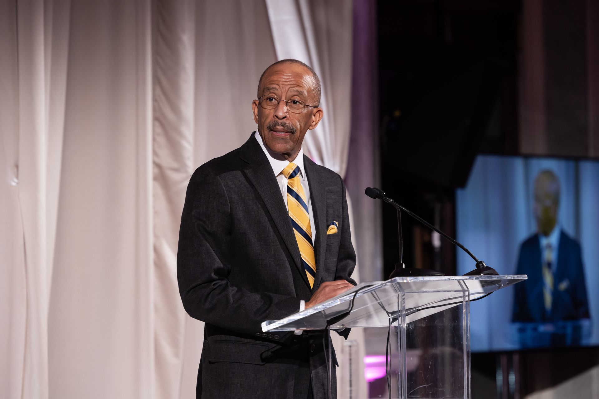 A man in a suit and tie is standing at a podium giving a speech.