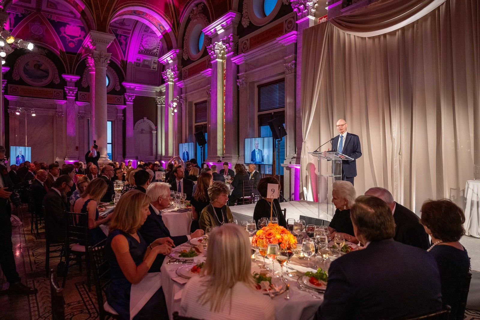 A man is giving a speech at a banquet in a large room.