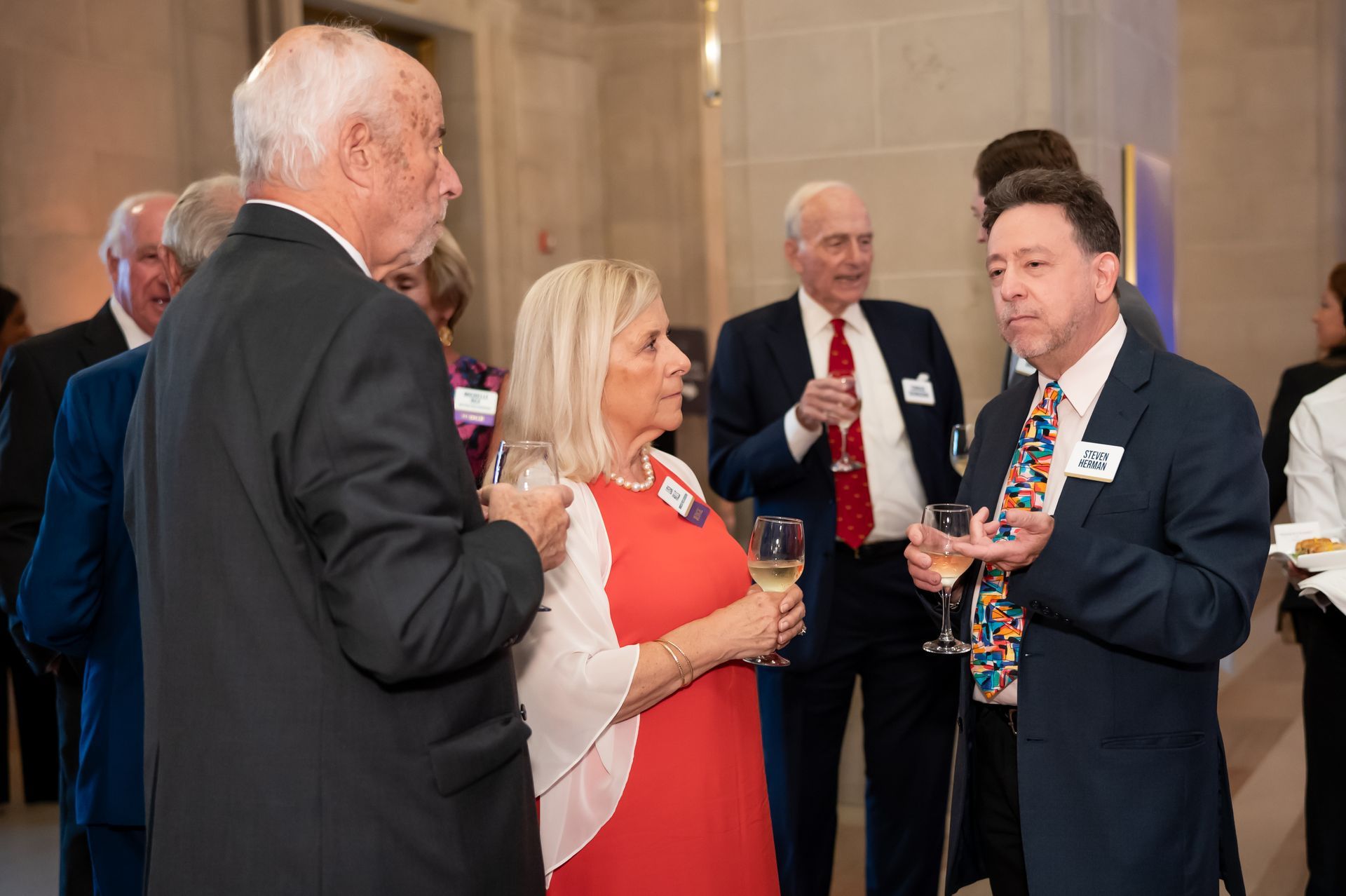 People conversing at a formal indoor event, holding drinks and name badges