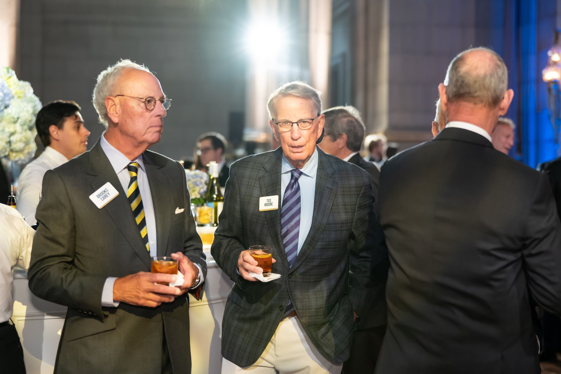 Three men in suits chatting with drinks at a formal indoor event