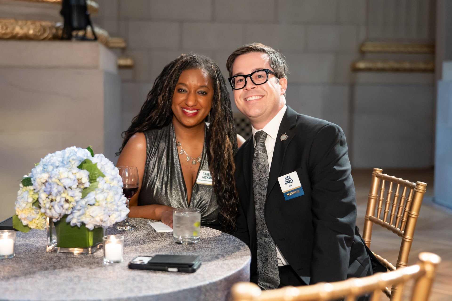 Two people smiling at a decorated table with flowers and drinks at an event.
