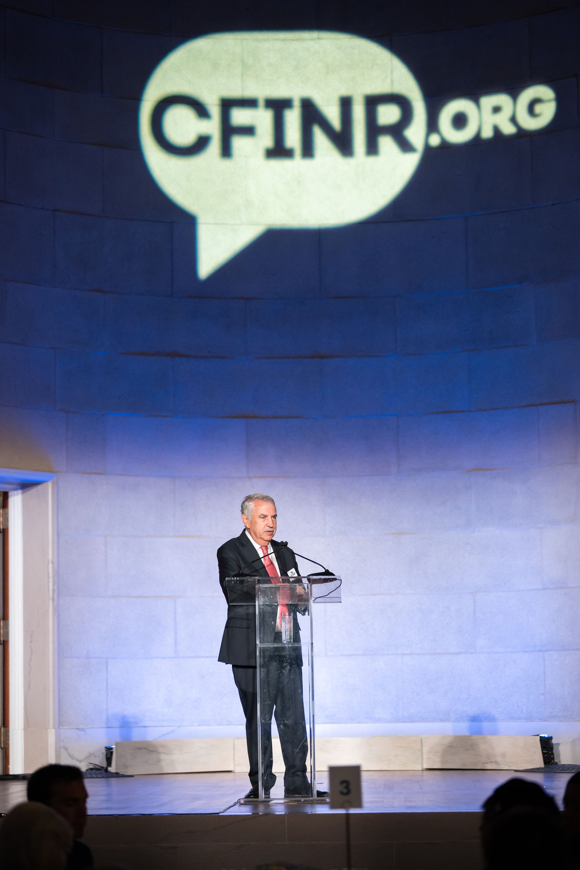 Speaker at podium on stage beneath a large CFINR.org logo