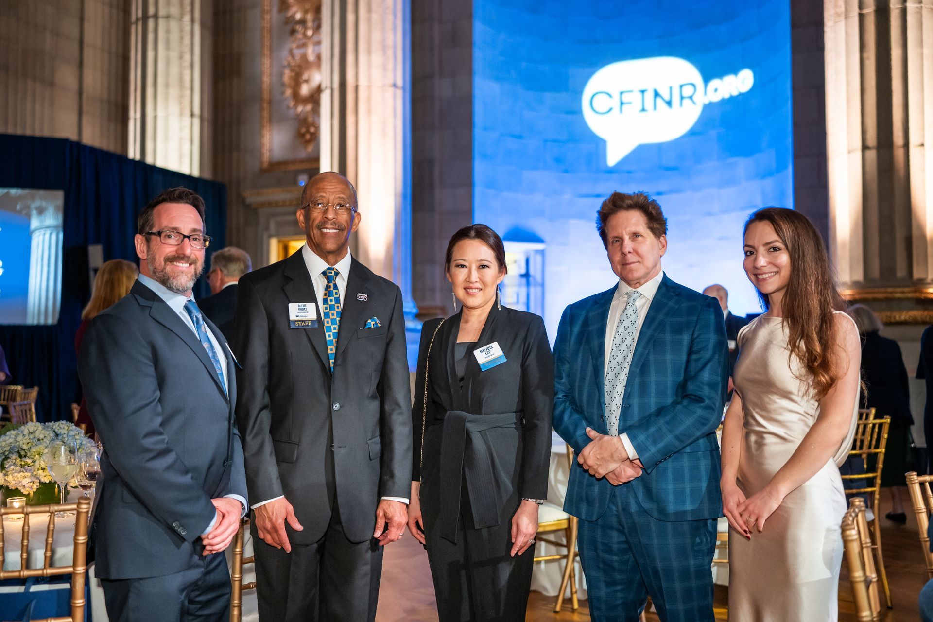 Five people posing at a CFNR event with a blue logo backdrop and formal attire.
