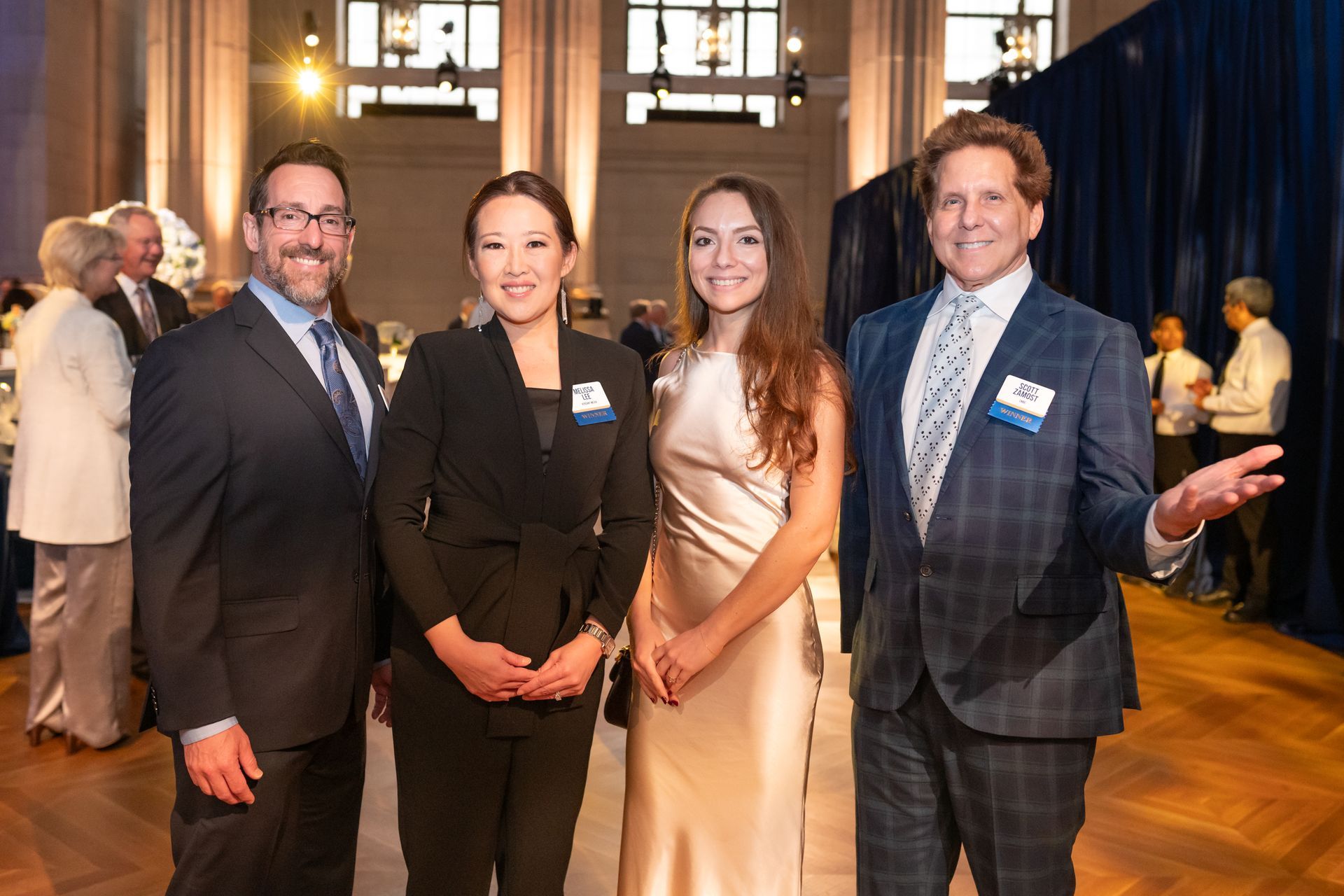Four people in formal attire smiling at a reception in a grand hall