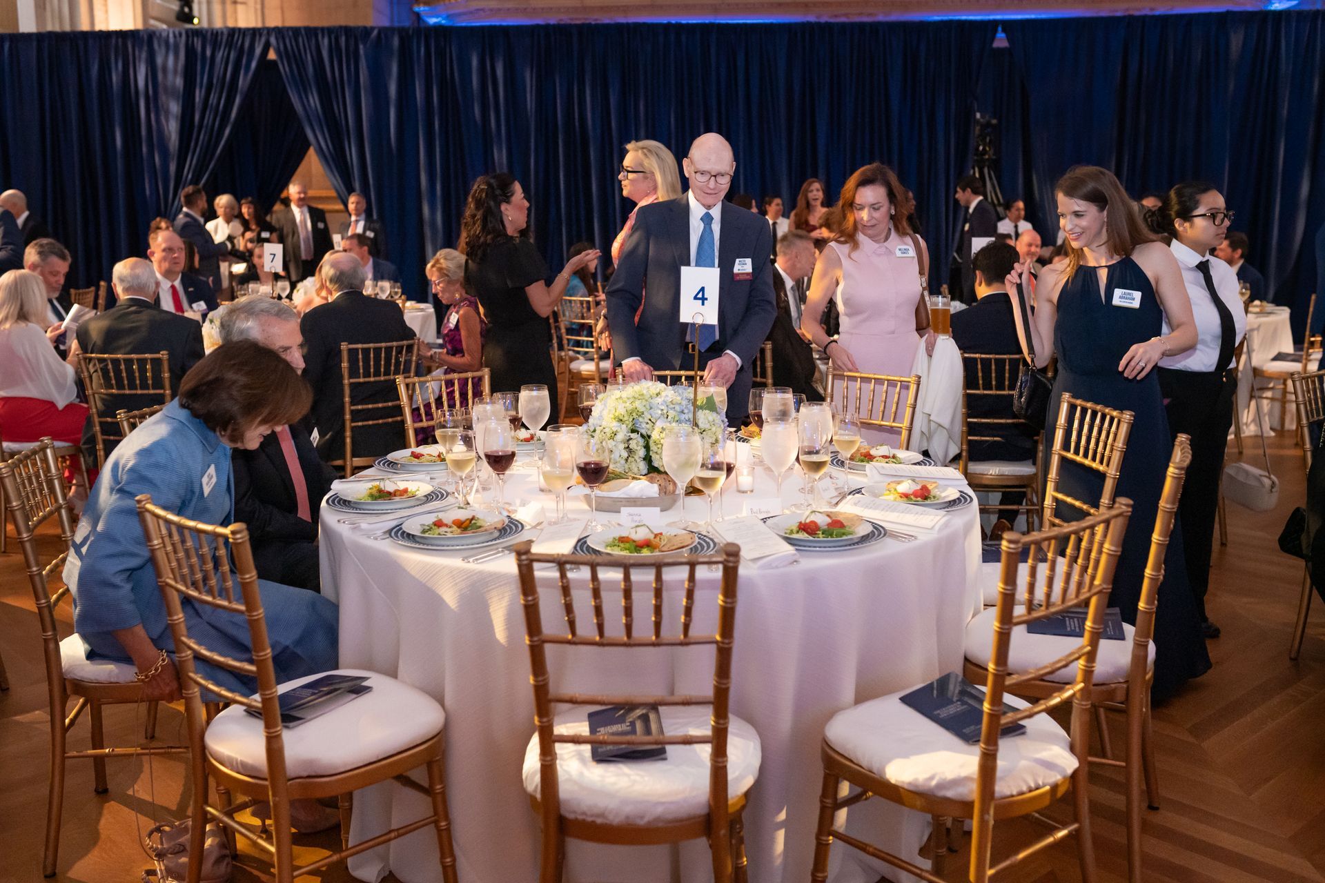 Round banquet table at a formal event, with people standing and seated in a ballroom.
