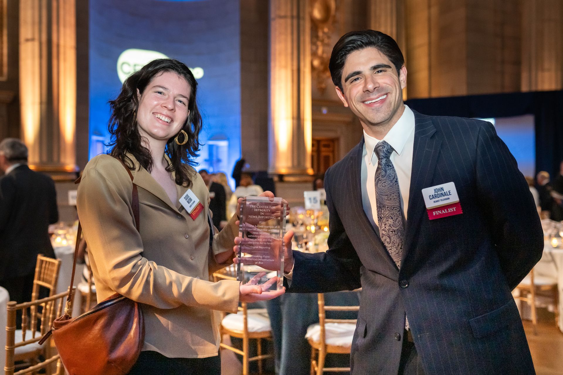 Two people in suits smiling and shaking hands at a formal event with a dessert table in the background