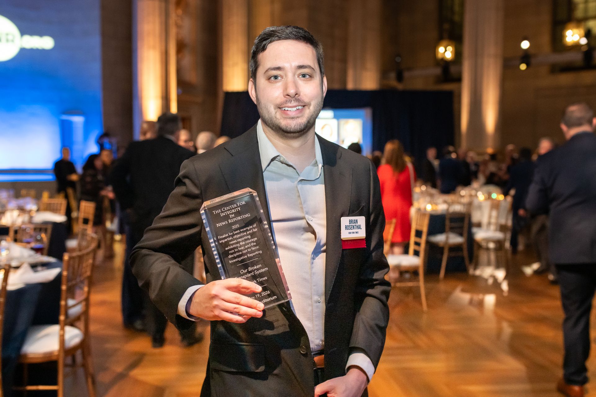 Man in a dark suit holding a glass award at a formal event banquet